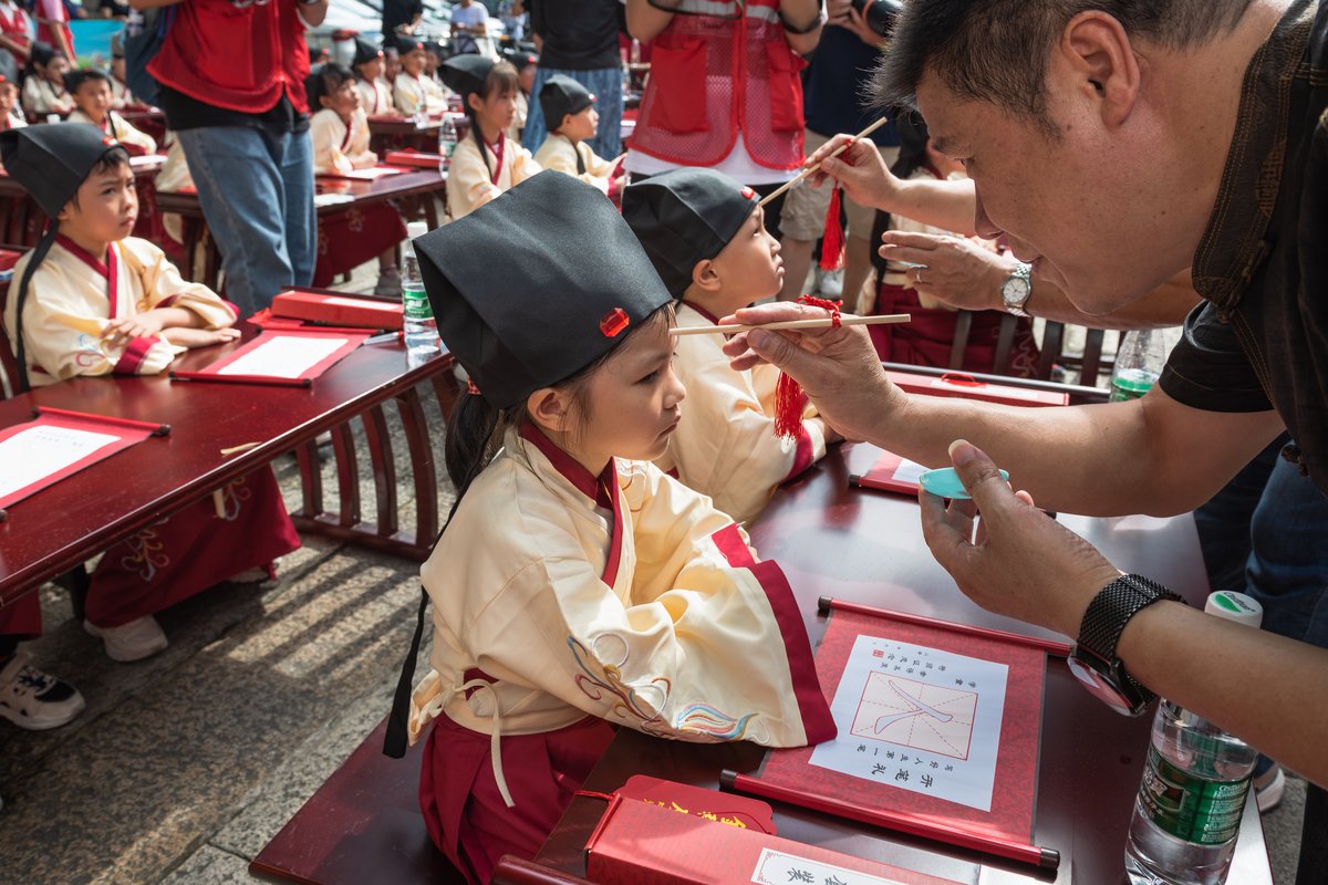 Honored guests from the village paint a red dot in the center of children’s foreheads to “enlighten” them according to folk beliefs, as “mole (痣)” sounds similar to “wisdom (智)”