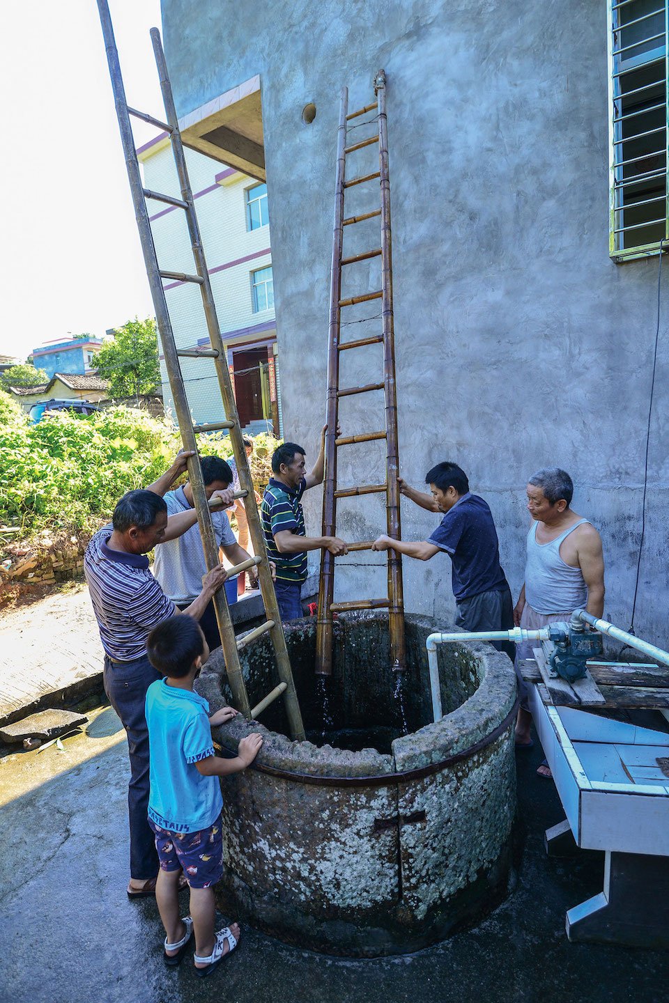 Elders and children are tasked with holding the ladder and cleaning up weeds at the mouth of the well