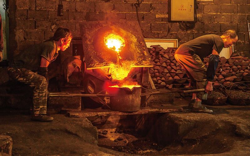 Chinese factory employees transfer molten iron into moulds.