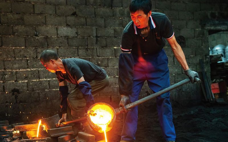 Two factory workers work with black iron.