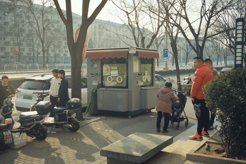 Unmasked pedestrians stroll by a closed down testing booth in Xicheng district, Beijing (Soth)