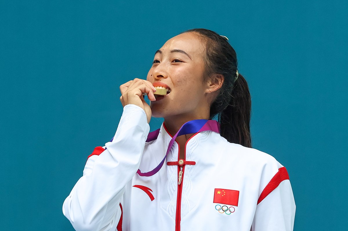 Chinese tennis star Zheng Qinwen biting a medal