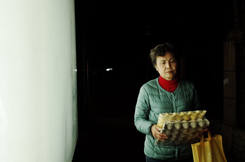 An older Chinese woman carrying eggs back, image from Nighttime Advertising Lightbox series