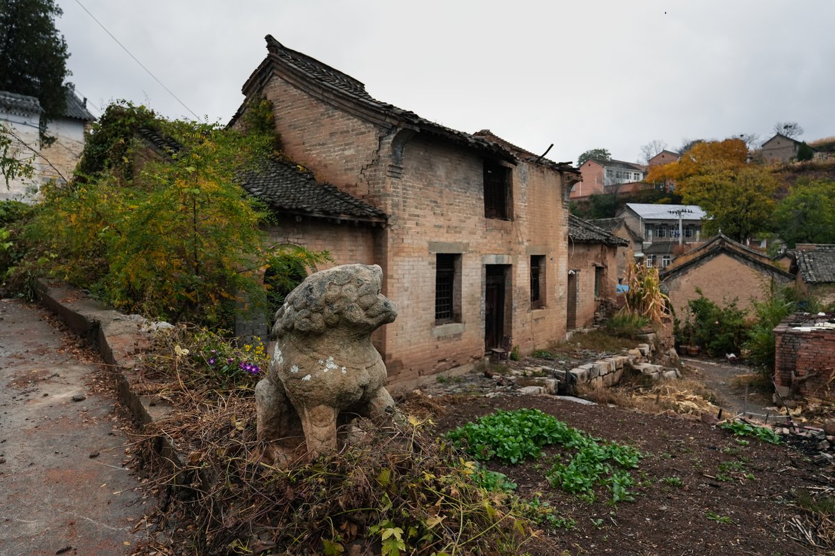 A stone lion stands alone by an abandoned house in Liangquan village, which, despite its wealth of cultural sites, receives very few visitors due to its remote location