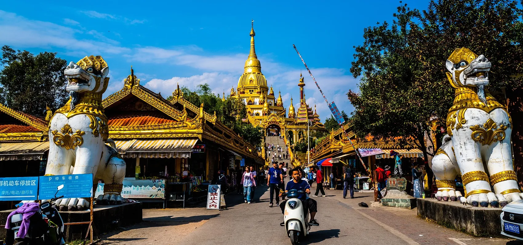 Scooters drive by entrance to Silver Pagoda in Mangshi, Yunnan province