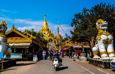Scooters drive by entrance to Silver Pagoda in Mangshi, Yunnan province