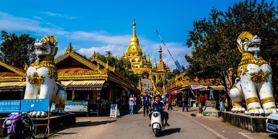 Scooters drive by entrance to Silver Pagoda in Mangshi, Yunnan province