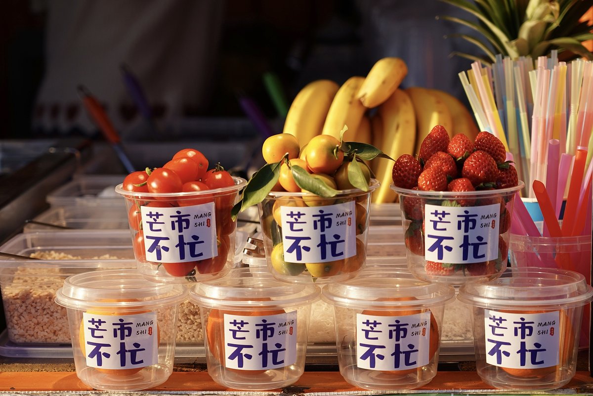 Market stalls selling fruit with the label Mangshi city slogan “Mangshi is not busy," eating in Mangshi Yunnan