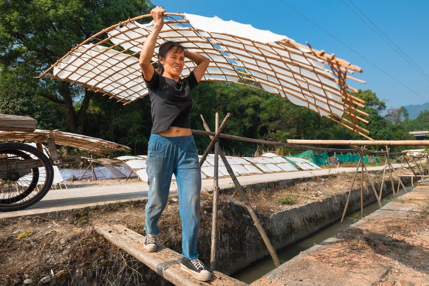 A worker holding thin sheets made of rice flour to dry in the sunshine in Shanfang Village, Guangdong province. The sheets are then cut into rice noodles. (2017)
