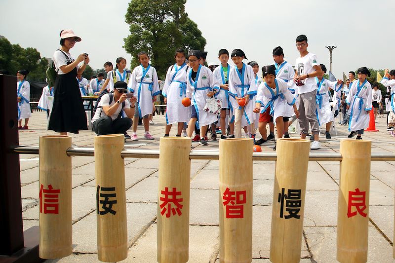 A group of Chinese kids dressed in traditional Chinese outfits playing a game of wood bowling.