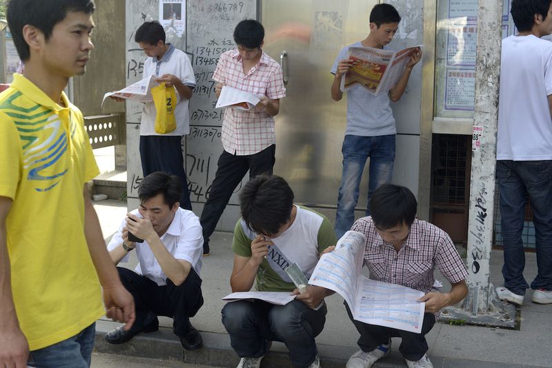 A group of Chinese men wait in line as they read documents