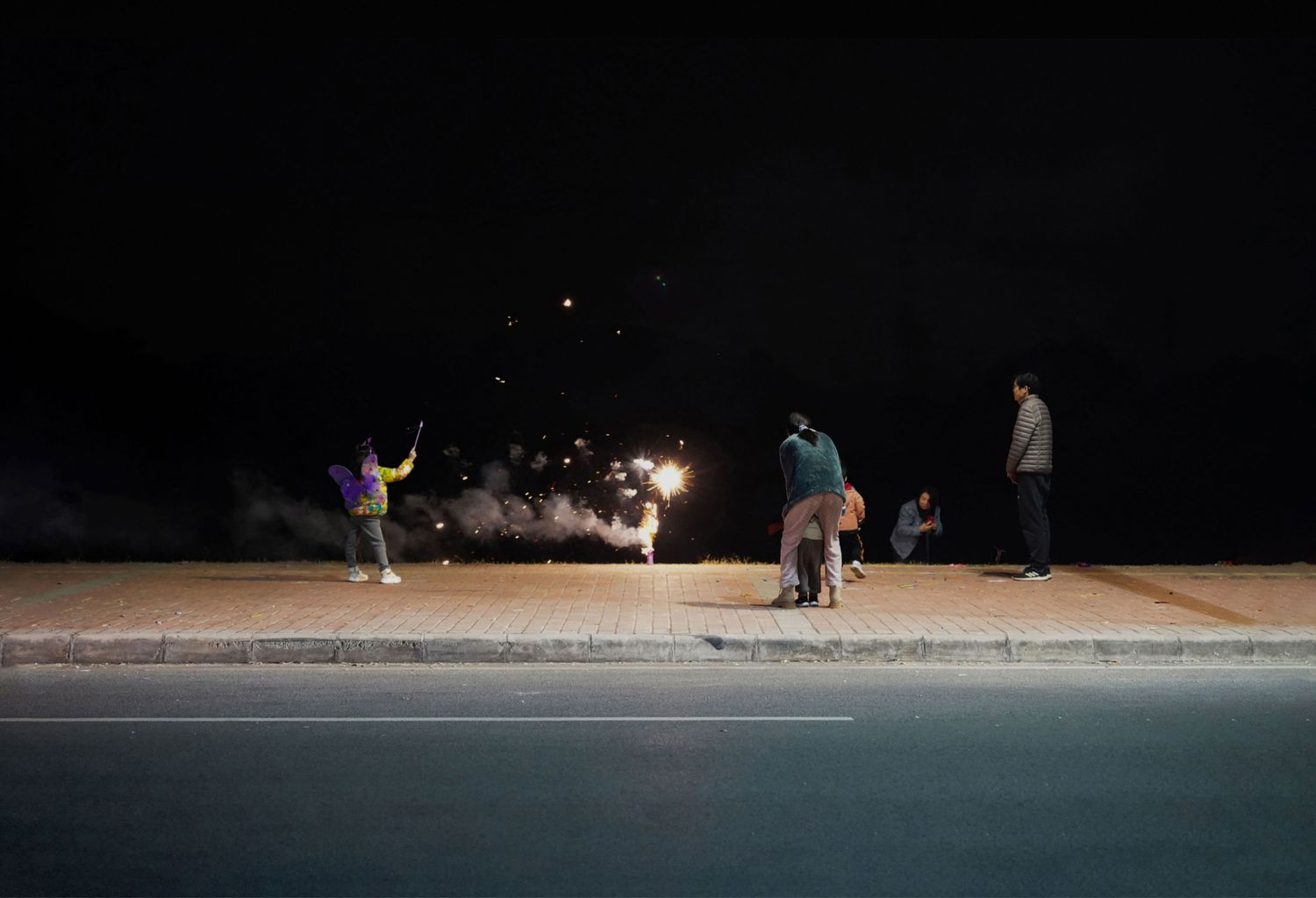 Family lighting up firecrackers next to the street, from Yan Jiacheng "Night in the Suburbs"