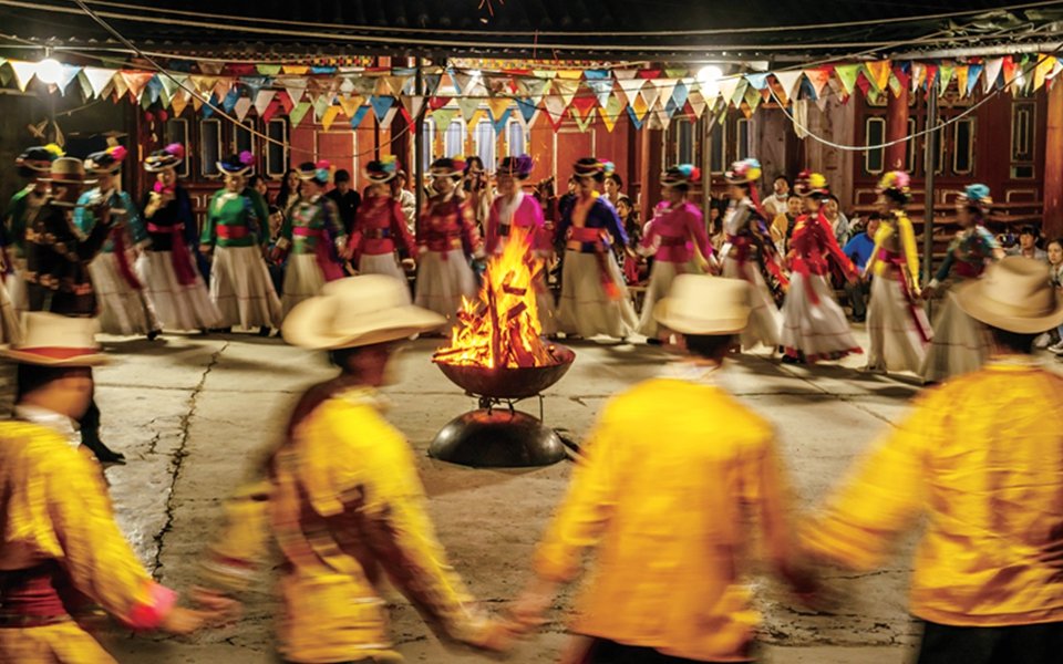 The Mosuo people give a performance with the men wearing yellow attire and women wearing multicolored outfits.