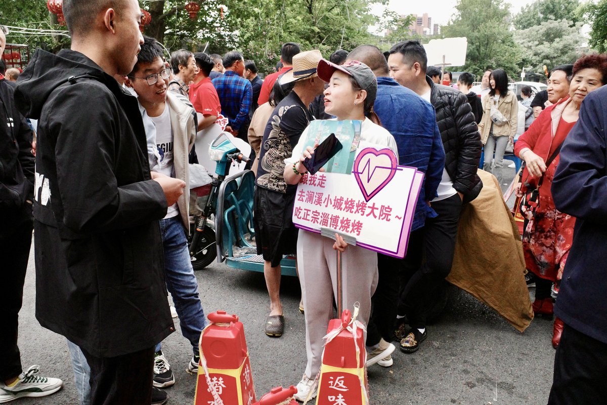 A woman holding an ad for a barbecue restaurant talking to potential customers