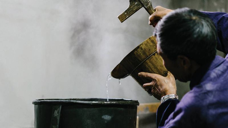 A Wangshengda employee adds cold water to the metal pot, part of the traditional process of distilling rice wine