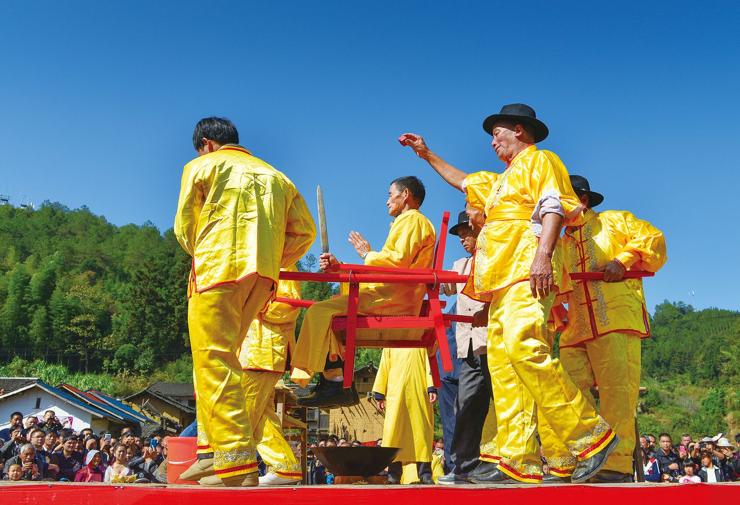 Four bearers carry one performer holding a sword in his hand in “sitting on the nail chair”