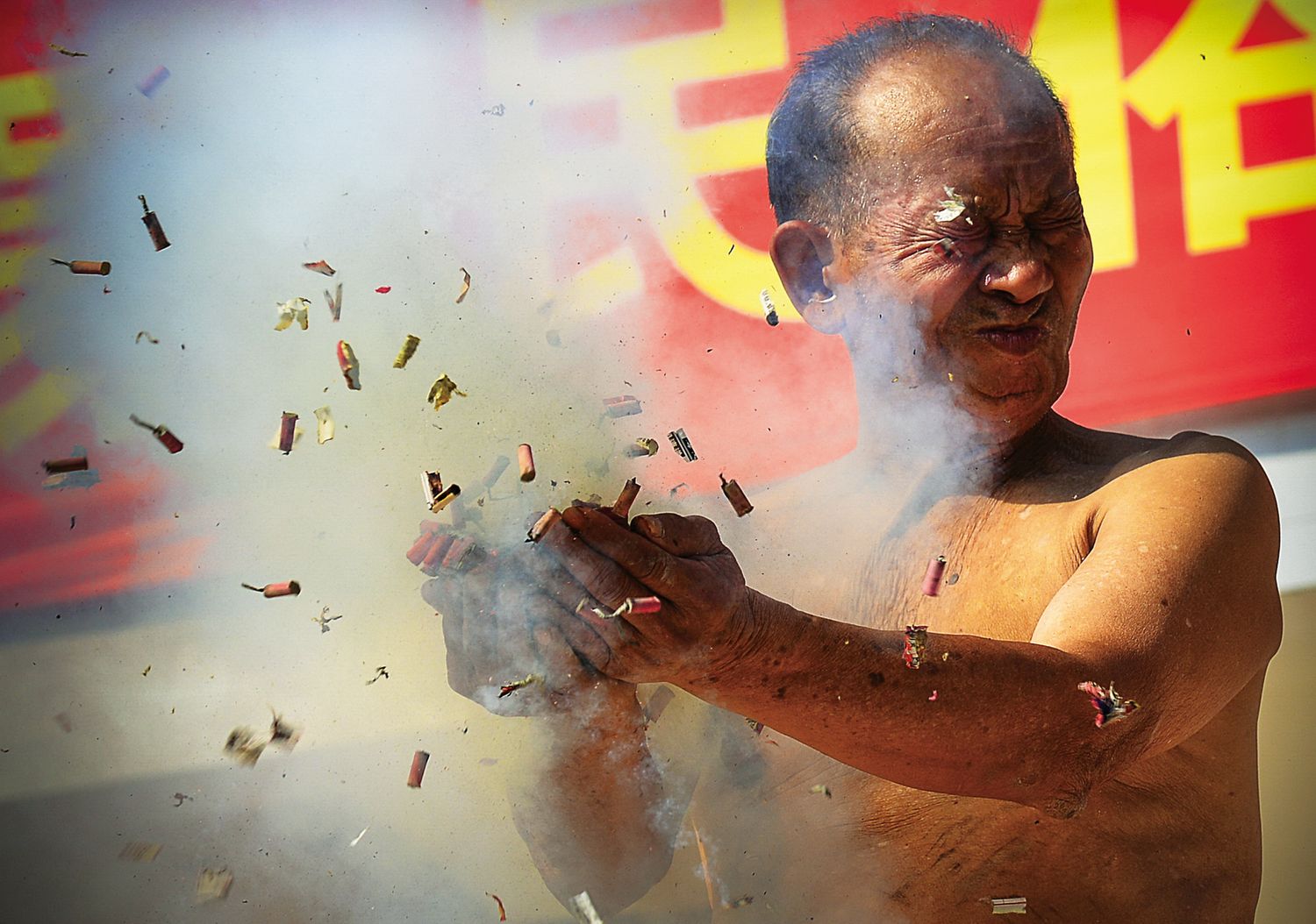 In “applauding the firecracker,” a bare-chested performer holds a firecracker in his hands as it explodes