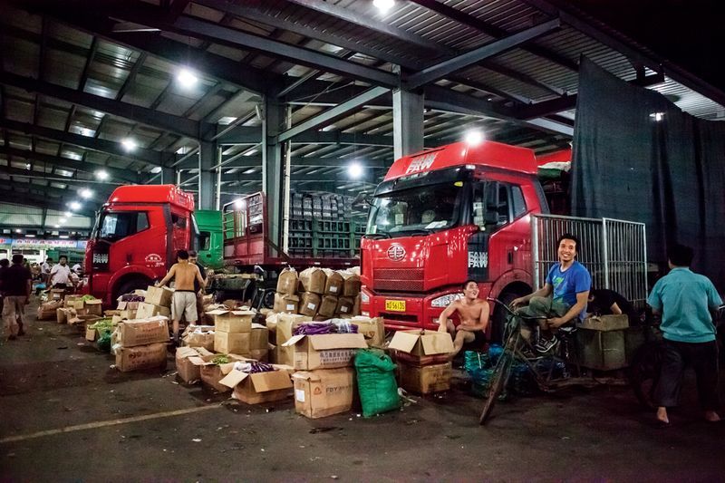 A delivery man waits for his coworkers to finish loading his cart before hauling the wares to be sold