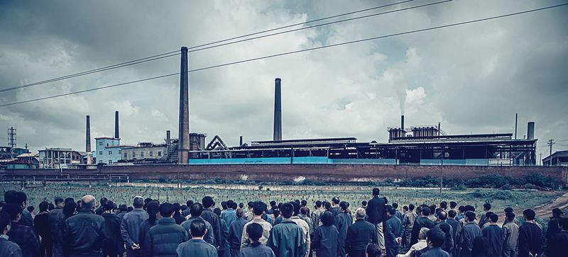 A crowd gathers outside the factory gates, where a body is discovered in the film&#x27;s opening scenes